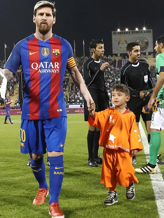 Bintang Barcelona Lionel Messi berjalan sambil menggandeng bocah Afghanistan, Murtaza Ahmadi (kanan) saat memasuki lapangan sebelum pertandingan persahabatan melawan Al-Ahli di ibu kota Qatar, Doha, Selasa (13/12). (Karim Jaafar/AFP)