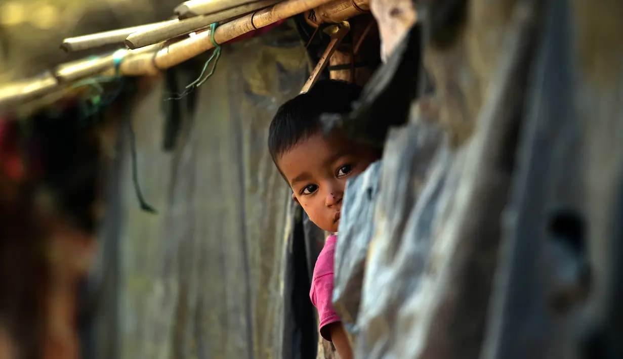 Seorang anak pengungsi muslim Rohingya melihat dari sebuah tenda di kamp pengungsi Thankhali di Distrik Ukhia, Bangladesh, (12/1). Sekitar 655.000 orang Rohingya melarikan diri ke Bangladesh sejak Agustus 2017 lalu. (Munir UZ ZAMAN/AFP)
