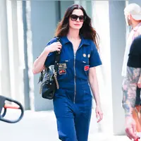 Anne Hathaway tampil mengenakan jumpsuit denim dengan aksen patch. Ia membawa Tas Valentino Garavani Panthea hitam yang  diperkenalkan dalam koleksi Fall Winter 2025/2026 bertajuk Le Méta-Théâtre Des Intimités oleh Creative Director Valentino, Alessandro Michele. [Dok. Valentino]