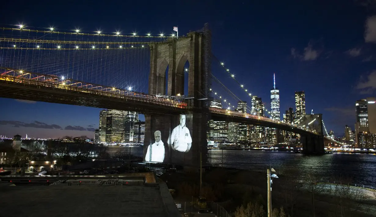 Gambar korban diproyeksikan pada Jembatan Brooklyn saat Hari Peringatan COVID-19 di Brooklyn, New York, Amerika Serikat, 14 Maret 2021. Kota New York yang mencatat kematian tertinggi akibat COVID-19 di AS, memberikan penghormatan yang emosional pada para korban yang meninggal. (Kena Betancur/AFP)