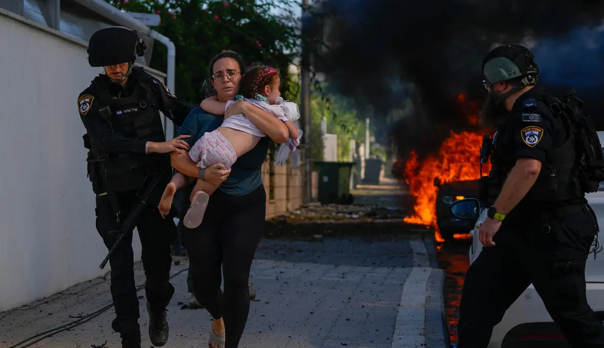 Petugas polisi mengevakuasi seorang wanita dan anak dari lokasi yang terkena roket yang ditembakkan dari Jalur Gaza di Ashkelon, Israel selatan, Sabtu, 7 Oktober 2023. (AP Photo/Tsafrir Abayov)