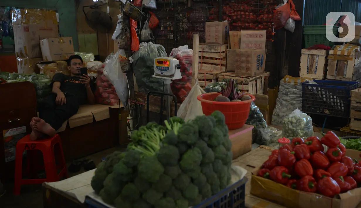 Seorang pedagang melihat ponselnya saat menunggu pembeli di di pasar Induk Kramat Jati, Jakarta, Rabu (7/4/2021).  Semua bahan pangan seperti cabai dan bawang akan stabil jelang puasa Ramadan dan Lebaran Idul Fitri 2021. (merdeka.com/Imam Buhori)