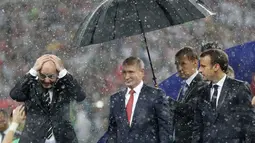Presiden FIFA Gianni Infantino menutupi kepalanya dengan tangan sementara Presiden Rusia, Vladimir Putin dilindungi payung saat hujan turun selama penyerahan medali dan trofi Piala Dunia 2018 di Stadion Luzhniki, Minggu (15/7). (AP/Matthias Schrader)