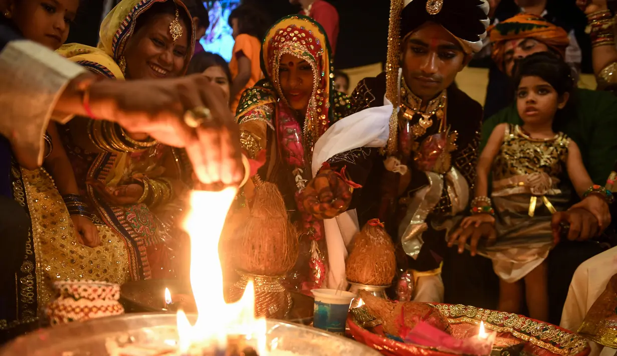 Sepasang pengantin menjalani ritual dalam prosesi pernikahan massal umat Hindu di Karachi, Pakistan, (19/3). Sebanyak 62 pasangan pengantin mengikuti pernikahan massal yang merupakan bagian dari perayaan Festival Holi. (AFP Photo /Asif Hassan)
