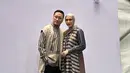 Fenita tampil anggun dengan gamis satin dan hijab gold. Arie Untung terlihat fashionable dengan kemeja lengan panjang dan sleeveles outer polos [@fenitarie]