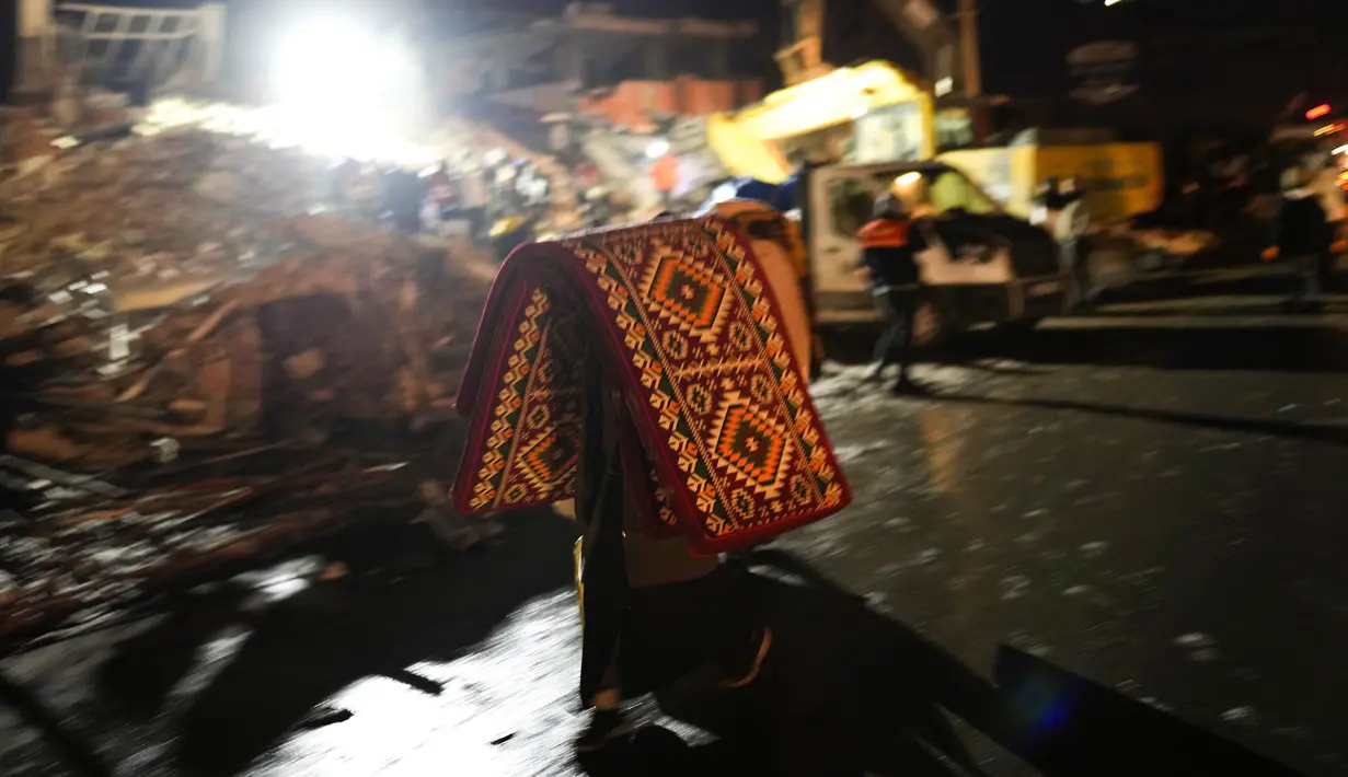 Seorang pria membawa selimut dan kasur saat tim penyelamat mencari korban gempa Turki di bangunan yang hancur di Elbistan, Turki selatan, Rabu, 8 Februari 2023. Tim penyelamat terkadang menggunakan ekskavator atau mengambil dengan hati-hati melalui puing-puing. Tidak jelas berapa banyak orang yang mungkin masih terjebak. (AP Photo/Francisco Seco)