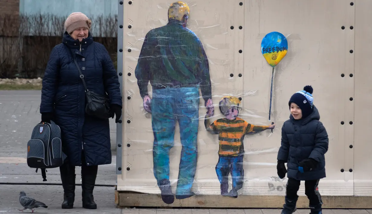 Orang-orang melewati karya seni dari seniman jalanan terkenal TvBoy yang dibuat pada dinding di Kota Bucha, Ukraina, 30 Januari 2023. Karya seni yang dibuat untuk menghormati para korban perang Rusia-Ukraina tersebut mengandung pesan kelahiran kembali dan harapan serta berharap agar konflik segera berakhir. (AP Photo/Efrem Lukatsky)