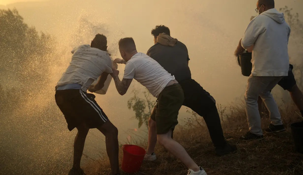 Penduduk setempat menggunakan ember berisi air untuk mencoba memadamkan api yang mendekati rumah mereka di Alcabideche, di luar Lisbon, Portugal, Selasa (25/7/2023). (AP Photo/Armando Franca)