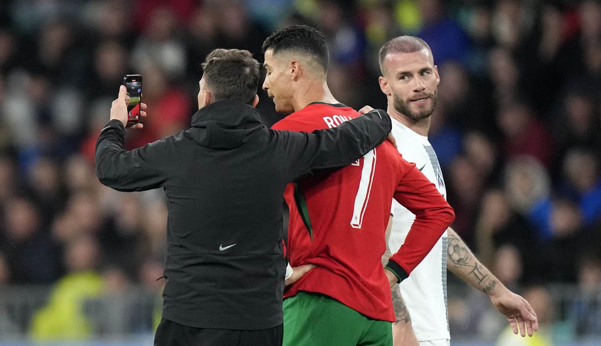 Pemain Portugal, Cristiano Ronaldo, pasrah berswafoto dengan fans saat melawan Slovenia pada laga persahabatan di Stadion Stozice, Ljubljana, Rabu (27/3/2024). (AP Photo/Darko Bandic)