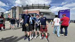 Suporter Skotlandia berpose di depan Gillette Stadium, Foxborough, Amerika Serikat, Jumat (19/6/2026), menjelang pertandingan melawan Maroko pada Piala Dunia 2026. Mereka mengenakan jersey Timnas Skotlandia, kilt tradisional, dan membawa bendera Saltire sebagai bentuk dukungan kepada tim berjuluk Tartan Army. (KLY Sports/Hery Kurniawan)