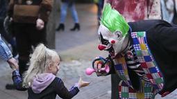 Seorang pria dengan kostum badut horor bermain dengan seorang gadis kecil sebelum Zombie Walk dan Parade Halloween tahunan di Essen, Jerman, Minggu (31/10/2021). Setiap 31 Oktober sebagian masyarakat dunia ikut memeriahkan perayaan Halloween. (AP Photo/Martin Meissner)