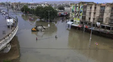 Orang-orang melintasi daerah banjir setelah hujan deras di Karachi, Pakistan, Minggu, (26/7/2020). Banjir melumpuhkan arus lalu lintas salah satu ruas jalan di Karachi. (AP Photo/Fareed Khan)