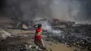 Seorang wanita berjalan tanpa alas kaki di dekat gubuk yang terbakar di daerah kumuh di Noida, pinggiran kota New Delhi, India, Minggu (11/4/2021). Dua anak tewas dan lebih dari 150 gubuk kumuh yang sebagian besar dihuni oleh para pemulung dalam kebakaran pada Minggu sore. (AP Photo/Altaf Qadri)