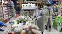 Seorang wanita mengenakan jas hujan dan masker membeli makanan di sebuah supermarket di Wuhan di provinsi Hubei, China tengah, Senin, (10/2/2020). China melaporkan kenaikan angka kematian akibat wabah virus corona. (Chinatopix via AP)