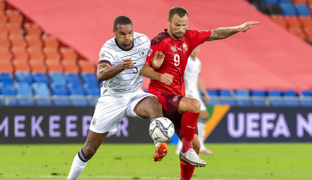 Pemain Jerman, Jonathan Tah, berebut bola dengan pemain Swiss, Haris Seferovic, pada laga UEFA Nations League di Stadion St. Jakob-Park, Senin, (7/9/2020). Kedua tim bermain imbang 1-1. (Georgios KefalasKeystone via AP)