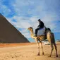 Seorang pria menunggang unta dengan latar belakang piramida Khafre yang berada di dataran tinggi Giza di pinggiran barat daya ibukota Kairo, Mesir (6/12). (AFP Photo/Mohamed El-Shahed)