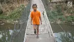 melintasi jembatan gantung semi permanen di kawasan Srengseng Sawah, Jakarta Selatan, Sabtu (24/8/2019). Jauhnya akses penyeberangan lain menyebabkan warga terpaksa memanfaatkan jembatan tersebut untuk menyeberangi Sungai Ciliwung. (Liputan6.com/Immanuel Antonius)