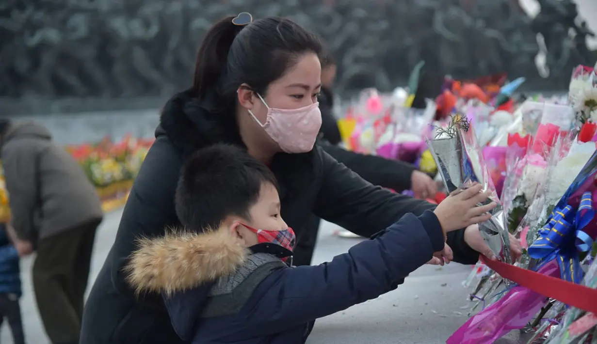 Seorang wanita dan seorang anak meletakkan karangan bunga saat memberi hormat di depan patung mendiang pemimpin Korea Utara Kim Il-sung dan Kim Jong-il pada peringatan 10 tahun kematian Kim Jong-il, Pyongyang, Korea Utara, 16 Desember 2021. Kim Jong-il adalah ayah dari Kim Jong-un. (KIM WON JIN/AFP)