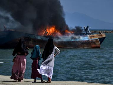 Para warga menyaksikan asap hitam mengepul dari kapal asing ilegal yang dibakar dan ditenggelamkan Kejaksaan Negeri Banda Aceh di perairan Pelabuhan Perikanan Samudera Kutaraja, Banda Aceh, Aceh, Kamis (18/3/2021). (AFP/Chaideer Mahyuddin)