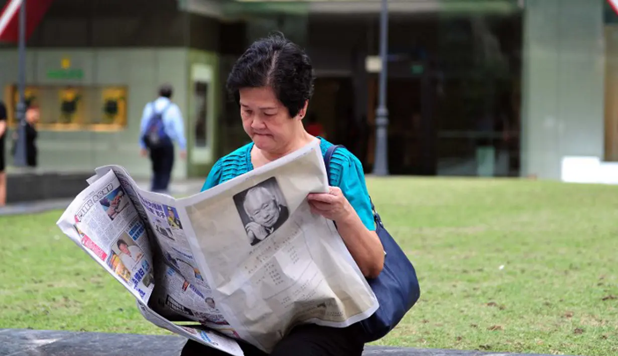 Seorang wanita membaca koran setelah sehari meninggalnya mantan PM Singapura, Lee Kuan Yew, Singapura, Selasa (24/3/2015). Lee meninggal pada hari Senin (23/3) di usia 91 tahun dan wajahnya menghiasi berbagai media cetak Singapura. (AFP PHOTO/Mohd FYROL)