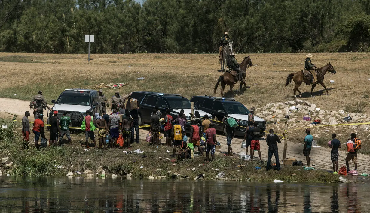 Petugas berusaha menahan para migran saat mereka menyeberangi Rio Grande dari Ciudad Acuña, Meksiko, ke Del Rio, Texas, Minggu (19/9/2021). Ribuan migran Haiti telah tiba di Del Rio, Texas, saat pihak berwenang berupaya menutup perbatasan untuk menghentikan arus migran.(AP Photo/Felix Marquez)