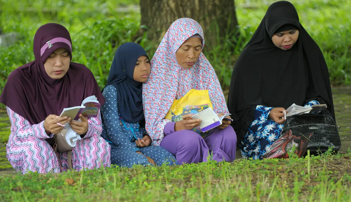 Sejumlah anggota keluarga membaca yasin di sebuah kuburan massal korban tsunami Aceh di Aceh, Senin (26/12). Warga memperingati 12 tahun pasca gempa dan tsunami Aceh dengan berziarah ke makam-makam massal korban. (CHAIDEER MAHYUDDIN/AFP)