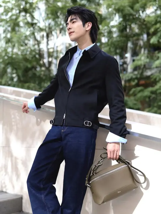 Mile Phakphum tampil dengan inner kemeja baby blue dipadukan jaket hitam serta celana denim, di tangannya membawa Dior Archie Bag hijau. [@milephakphum]