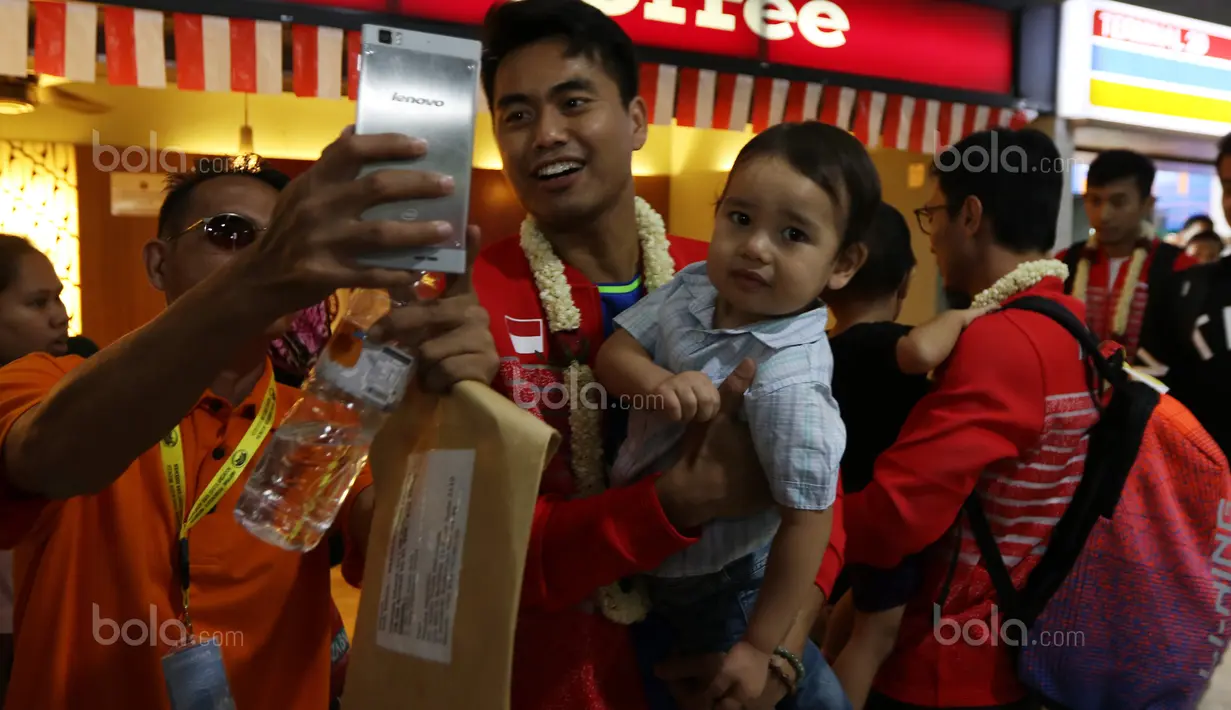 Tontowi Ahmad menggendong anak dan menlayan foto bersama fans saat tiba di Bandara Soekarno-Hatta, Cengkareng (29/8/2017). Tontowi/Liliyana meraih medali emas pada kejuaraan dunia di Glasgow. (Bola.com/Nicklas Hanoatubun)