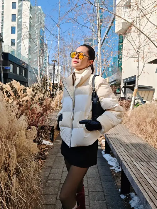 Ia padukan turtleneck berlapis puffer jacket putih dipadu dengan rok mini dan stocking hitam. Lengkapi busananya, ia kenakan boots cokelat dan shoulder bag hitam [@miktambayong]