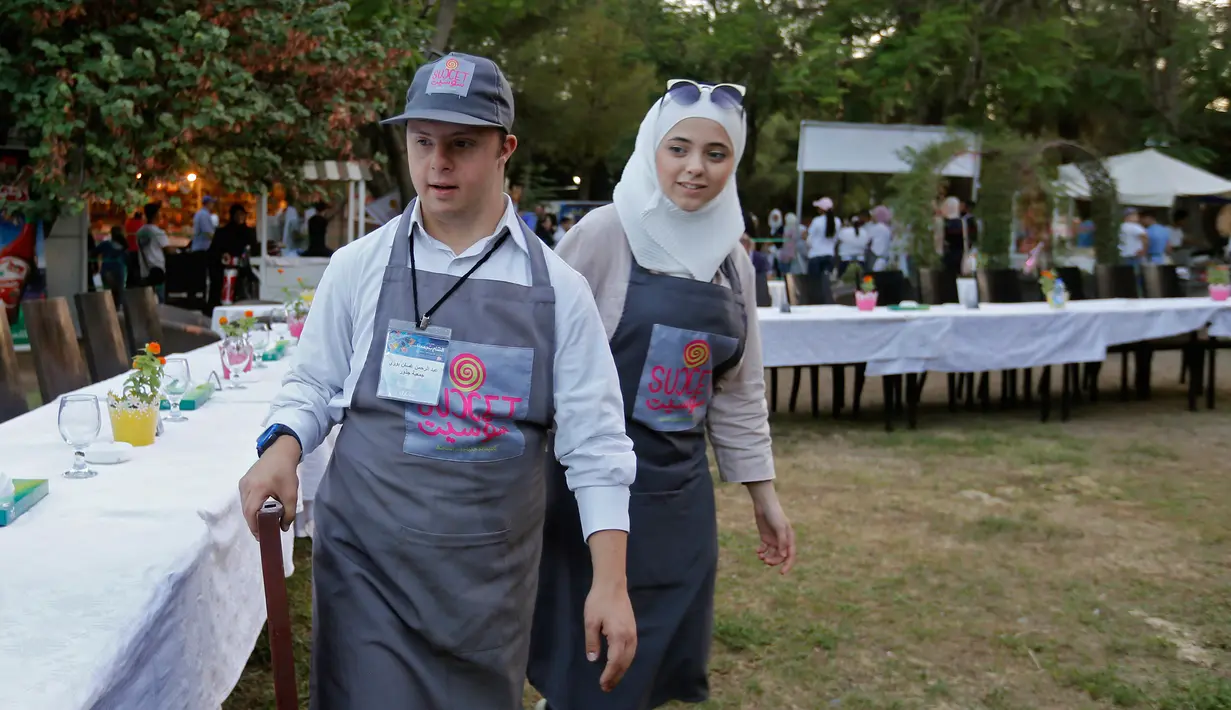 Dua anak down syndrome Abdel Rahman saat bekerja di kedai kopi Sucet  selama festival "Sham gather us" di Damascus (11/7). Enam belas anak laki-laki dan perempuan down syndrome bekerja di Cafe Sucet melayani pelanggan. (AFP Photo/Louai Beshara)
