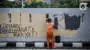Petugas PPSU membersihkan coretan yang mengotori pembatas jalan pascaunjuk rasa di kawasan DPR/MPR, Jakarta, Jumat (17/7/2020). Coretan tersebut dilakukan oleh massa yang menolak RUU Omnibus Law Cipta Lapangan Kerja di depan Gedung DPR pada Kamis (16/7) kemarin. (Liputan6.com/Faizal Fanani)