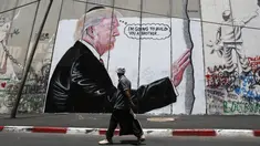 Seorang pria Palestina berjalan didepan grafiti yang menggambarkan Presiden AS Donald Trump di tembok pemisah Israel - Palestina di kota Bethlehem (4/8). Tembok di Tepi Barat ini membentang sepanjang 700 kilometer. (AFP Photo/Musa Al Shaer)