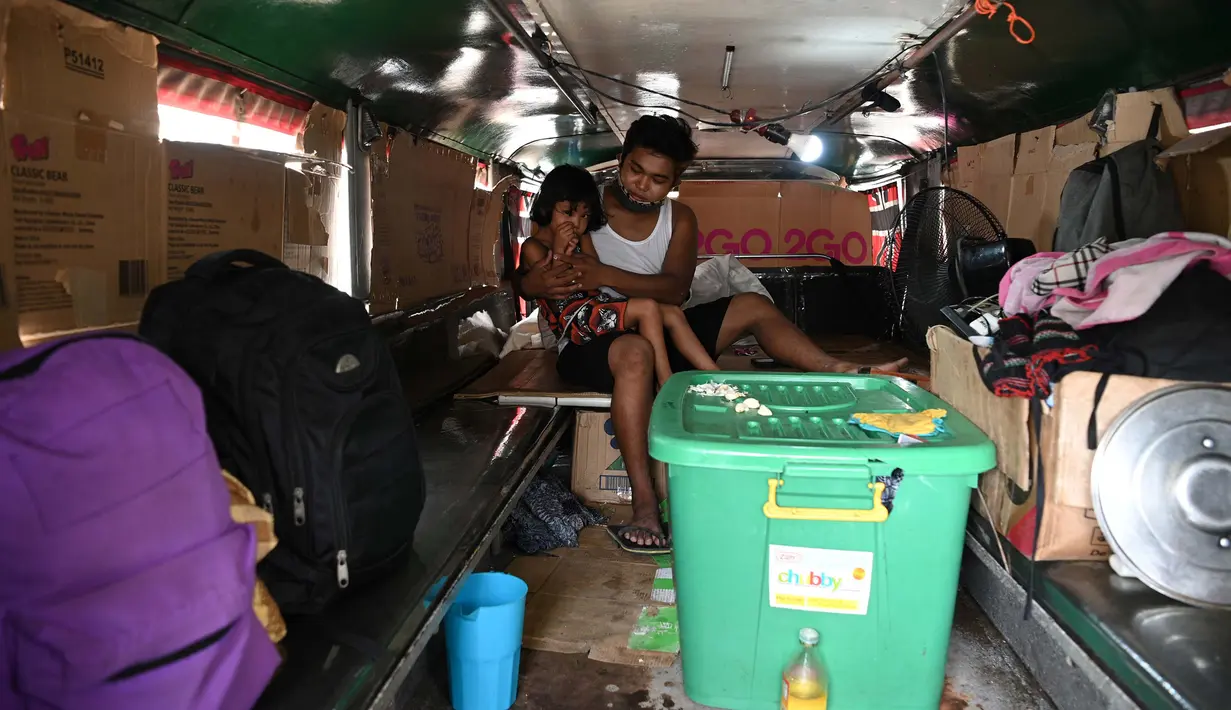 Daniel Flores bersama salah satu anaknya di dalam jeepney mereka yang berfungsi sebagai rumah sementara di Manila, 12 Agustus 2020. Angkutan ikonik di Filipina itu belum dapat mengangkut penumpang sejak Maret akibat lockdown Covid-19 yang membuat jutaan orang kehilangan pekerjaan. (Ted ALJIBE/AFP)