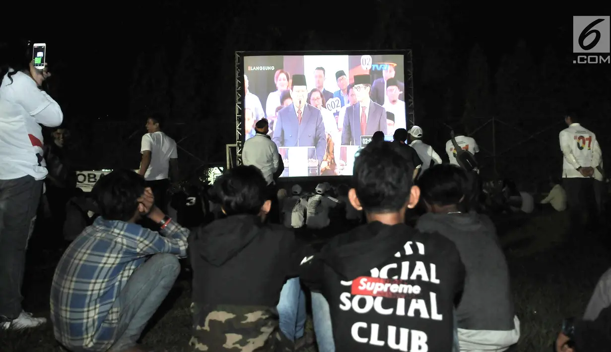 Para pendukung Capres dan Cawapres nomor urut 01 dan 02 saat nonton bareng Debat Perdana Pilpres di kawasan Gedung Bidakara, Jakarta, Kamis (17/1). Mereka menonton lesehan dengan layar tancap yang disediakan warga sekitar. (merdeka.com/Iqbal S Nugroho)