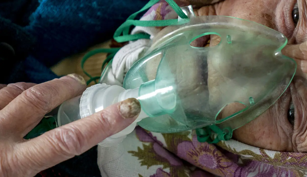 Seorang wanita lanjut usia yang menderita COVID-19 bernapas dengan oksigen di sebuah rumah sakit di Pochaiv, Ukraina, 1 Mei 2020. Total kasus COVID-19 di Ukraina sebanyak 201.305 kasus, 3.996 kematian, dan 88.453 orang telah pulih. (AP Pohto/Evgeniy Maloletka)