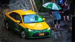 Seorang pejalan kaki menghentikan taksi saat hujan deras di Bangkok (23/9/2020). (AFP/Mladen Antonov)