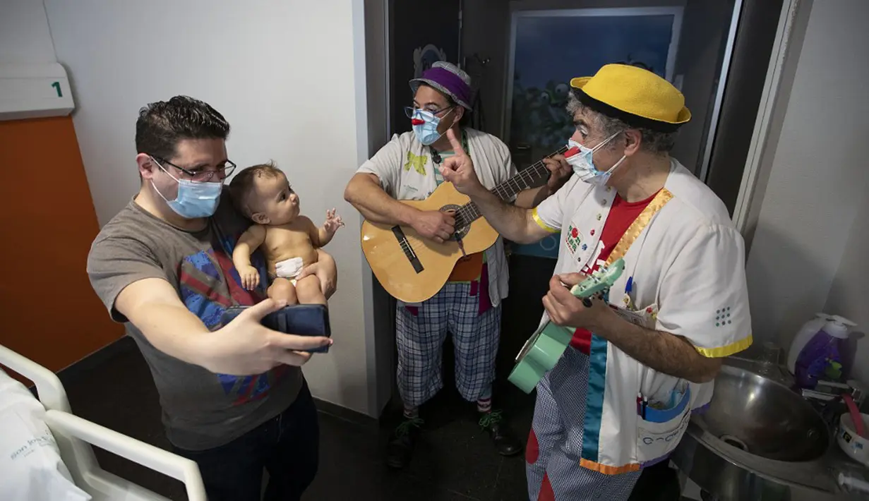 Badut dari LSM Media Sunrise (Senyuman Medis) tampil untuk pasien berusia satu tahun Eressea dan ayahnya di sayap anak-anak Rumah Sakit Son Espases, Palma de Mallorca, Spanyol, 8 Maret 2021. (JAIME REINA/AFP)