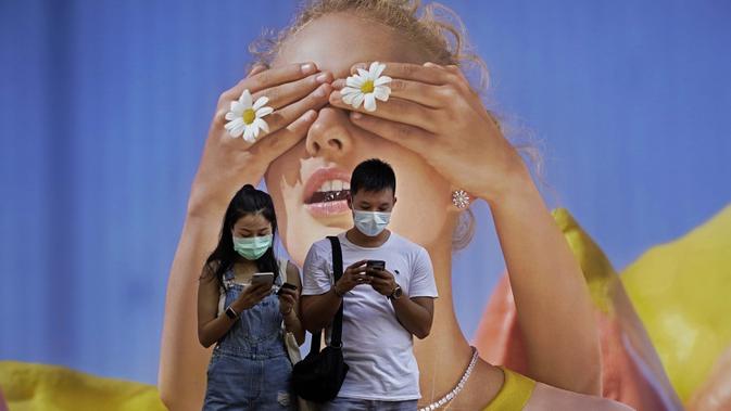 Pasangan yang memakai masker melihat ponsel mereka di depan poster besar di Hong Kong pada 27 Juli 2020. (AP Photo / Vincent Yu)