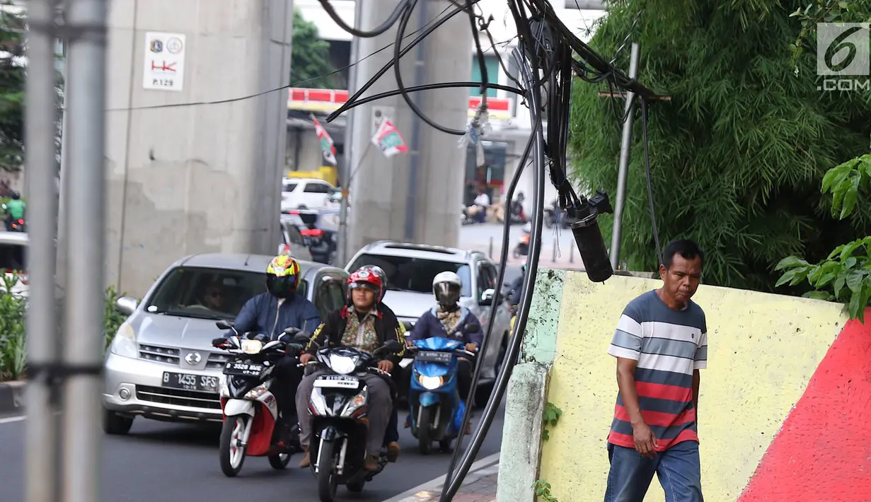 Pejalan kaki melintasi trotoar yang terhalang instalasi kabel di Jalan Kyai Maja, Jakarta, Rabu (10/4). Selain menganggu kenyamanan pejalan kaki, kondisi instalasi kabel yang semrawut tersebut juga berbahaya apabila mengandung aliran listrik. (Liputan6.com/Immanuel Antonius)