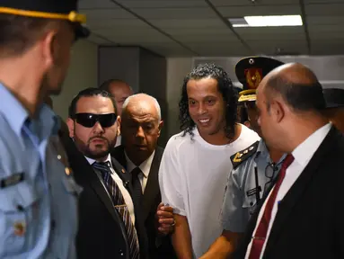 Mantan pemain Barcelona asal Brasil, Ronaldinho (tengah) tiba di Asuncion's Justice Palace untuk bersaksi tentang masuknya dia yang tidak teratur ke negara itu, di Asuncion, pada 6 Maret 2020. Ronaldinho mengumumkan dirinya positif Covid-19 pada Minggu (25/10/2020) malam WIB. (AFP/Norberto Duarte)