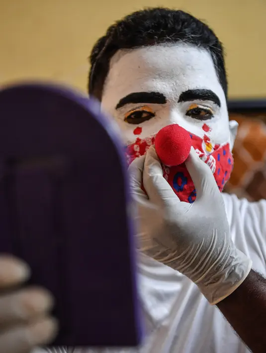 Relawan pekerja sosial Ashok Kurmi, mengenakan hidung badut sebelum menyebarkan kesadaran tentang COVID-19 di daerah kumuh Mumbai pada 2 Juni 2021. Kurmi turun tangan memerangi virus Corona di daerah kumuh Mumbai menggunakan aksesori yang tidak biasa, yaitu kostum badut. (INDRANIL MUKHERJEE/AFP)