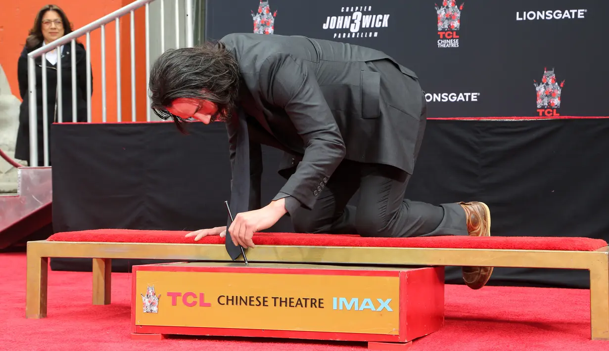 Aktor Keanu Reeves membubuhkan tanda tangan dalam upacara pembuatan cetakan tangan dan kaki di TCL Chinese Theatre, Los Angeles, Selasa (14/5/2019). Aktor 54 tahun itu mendapat penghargaan membuat cetakan tangan dan kaki untuk merayakan keberhasilan karirnya dalam film. (Willy Sanjuan/Invision/AP)
