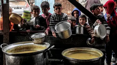 Anak-anak menunggu sambil memegang panci kosong bersama pengungsi Palestina lainnya untuk mendapatkan makanan menjelang berbuka puasa selama bulan suci Ramadhan, di Rafah di Jalur Gaza Selatan pada 16 Maret 2024. (SAID KHATIB/AFP)