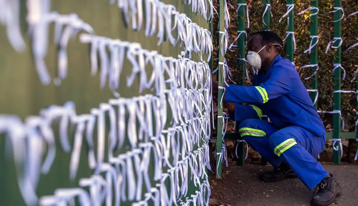 Silva Cossa, seorang pengurus, mengikat pita ke pagar gereja St James Presbyterian di Bedford Gardens, Johannesburg, Rabu (29/7/2020). Pita tersebut mewakili warga Afrika Selatan yang meninggal akibat virus corona COVID-19. (AP Photo/Themba Hadebe)
