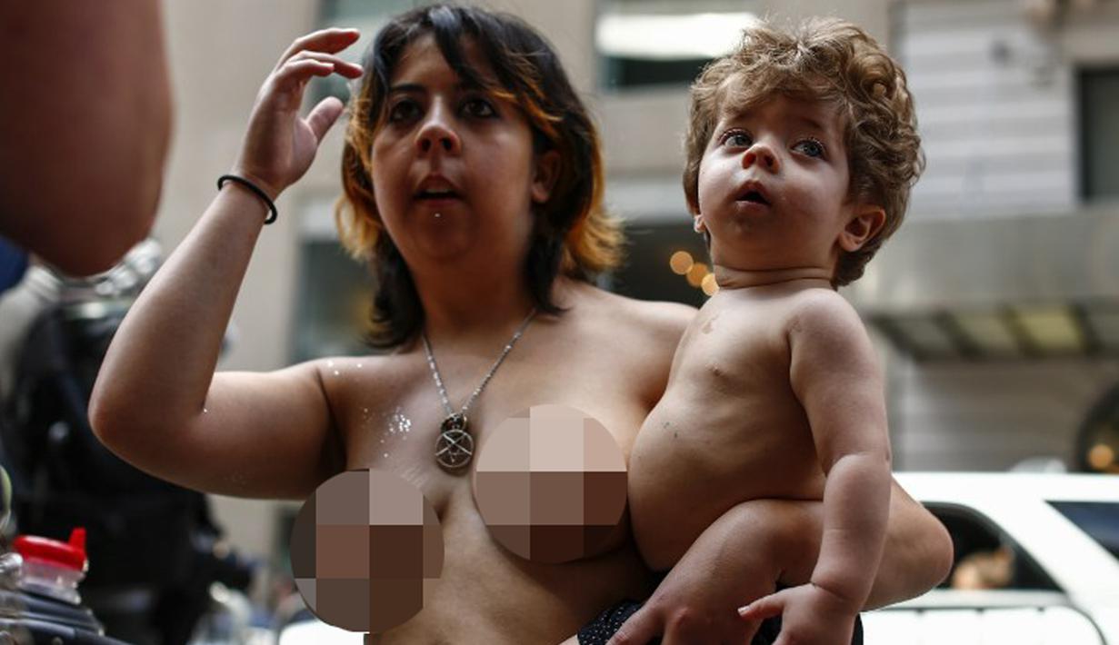 Seorang wanita sambil mengendong anaknya berpartisipasi dalam parade GoTopless di Manhattan, New York City, Minggu (23/8/2015). Aksi tersebut menuntut persamaan hak untuk bertelanjang dada seperti pria. (Kena Betancur/Getty Images/AFP)