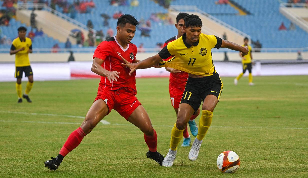 Gelandang Timnas Indonesia U-23, Asnawi Mangkualam berusaha merebut bola dari bek Malaysia, Muhammad Safwan bin Mazlan dalam pertandingan perebutan medali perunggu SEA Games 2021 di Stadion My Dinh, Minggu (22/5/2022). Indonesia ditahan imbang 1-1 dan menang 4-3 di adu penalti. (AFP/Tang Chhin Sothy)