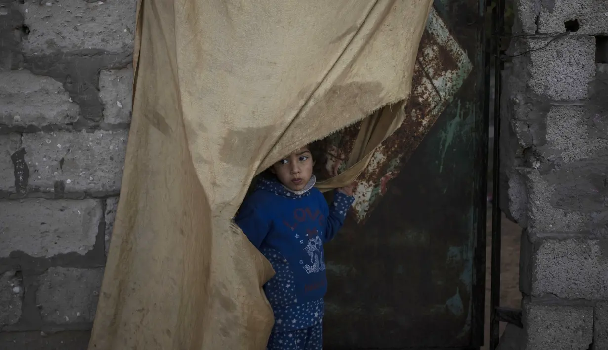 Seorang gadis Palestina berdiri di luar rumah keluarganya saat cuaca dingin di daerah kumuh di pinggiran kamp pengungsi Khan Younis, Jalur Gaza selatan pada Rabu, 19 Januari 2022. (AP Photo/Khalil Hamra)