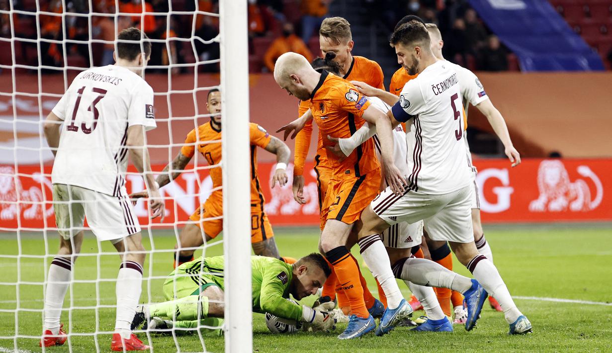 Kiper Latvia, Roberts Ozols (bawah) menangkap bola dari ancaman pemain Belanda dalam laga Kualifikasi Piala Dunia 2022 Zona Eropa Grup G di Johan Cruijff Arena, Amsterdam, Sabtu (27/3/2021). Belanda menang 2-0 atas Latvia. (AFP/Maurice van Steen/ANP)