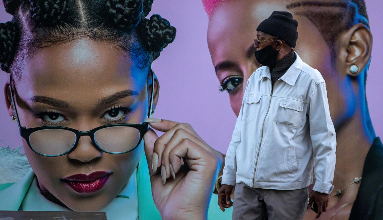 Seorang pria yang mengenakan masker berdiri di depan papan iklan produk rambut di Soweto, Afrika Selatan, Senin (29/6/2020). (AP Photo/Themba Hadebe)