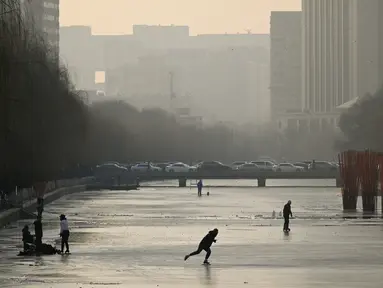 Sejumlah warga bermain ice skating di sungai yang membeku di Beijing, China (10/1). Akibat membeku, Sungai ini menjadi objek wisata dadakan. (AFP Photo/Wang Zhao)